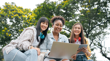 Fototapeta na wymiar Diversity woman group happy friends searching media content online using laptop sitting in the park. looking online lessons on laptop with her friends at park. Prepare for college university concept.