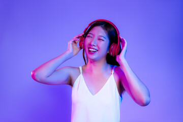 Young asian woman in white tank top wearing red headphone listen to music on the purple neon light...