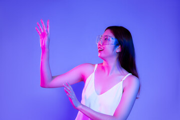 Young asian woman in white tank top wearing vr glasses posing touching on the bllue color background.
