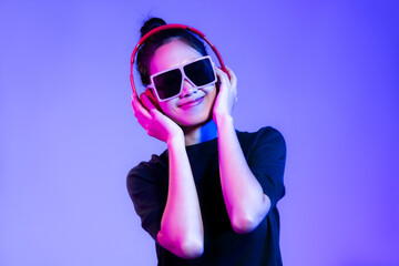 Young asian girl in black t-shirt wearing sunglasses and red headphones listen to music and dancing on purple background. 
