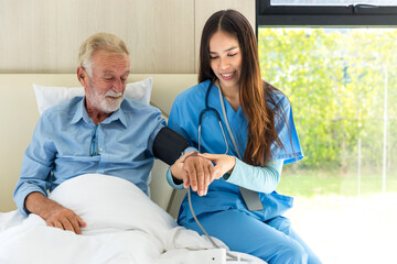 Caregiver nurse using blood pressure monitor to Senior patient sit on Bed. Nurse helping senior Man