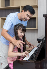 Father and daughter at home playing music on a piano. Dad and daughter are playing the piano. Pianist teacher teaching girl kid student to play piano, music education concept.