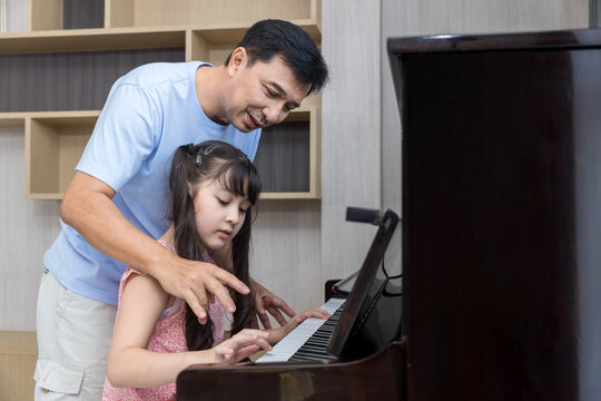 Father And Daughter At Home Playing Music On A Piano. Dad And Daughter Are Playing The Piano. Pianist Teacher Teaching Girl Kid Student To Play Piano, Music Education Concept.