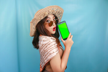 Young Asian happy woman showing green screen on her smartphone isolated by a blue background