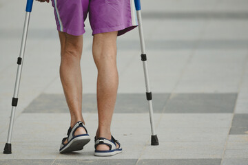 Disable man using crutches to walk for rehab.Patient with leg injury during training with crutches.Old man walking on the street for outdoor exercise.