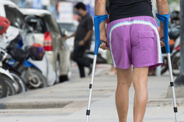 Disable man using crutches to walk for rehab.Patient with leg injury during training with crutches.Old man walking on the street for outdoor exercise.