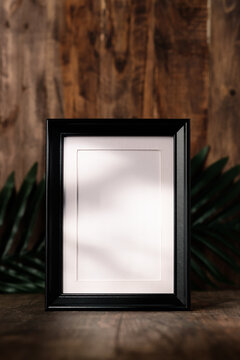 blank black photo frame on wood table and wall witn sunlight from window