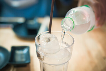 Hand holding blue water bottle pouring water into the glass on blurry natural green tree background.Health care food and drink concept.