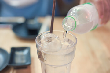 Hand holding blue water bottle pouring water into the glass on blurry natural green tree background.Health care food and drink concept.
