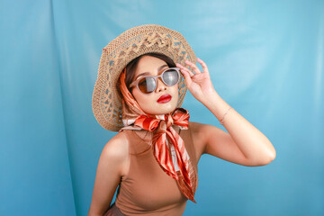 Young Asian confident and happy woman holding her sunglasses isolated by a blue background.