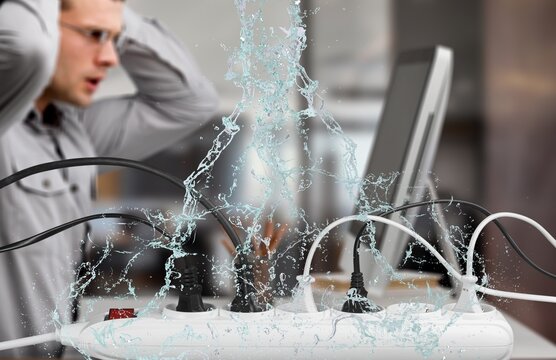 A Bank Of Plugs On A Desk With Water Leaks Falling Next To A Man Working In Danger Of Electrocution At Home Or Office Concept