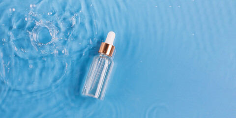 Naklejka premium Glass bottle of anti aging serum and falling water drops on blue background. Facial serum mockup. Copy space.