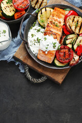 Salmon steak with vegetables and white sauce on dark background.