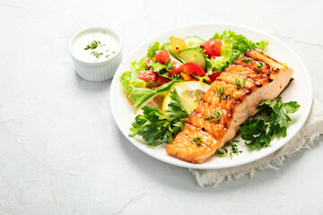 Salmon steak with vegetables and fries on light background.