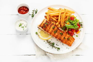 Salmon steak with vegetables and fries on light background.