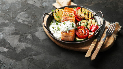 Salmon steak with vegetables and white sauce on dark background.