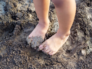 Dirty bare foot child with mud in nature background. Kid playing in mud pit outdoor. Concept of learning nature, fun freedom playing, family activity outdoor, ef learning, skin health care.