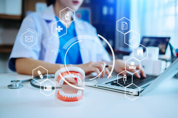 Concentrated dentist sitting at table with jaw samples tooth model and working with tablet and laptop in dental office professional dental clinic. with virtual icon hologram
