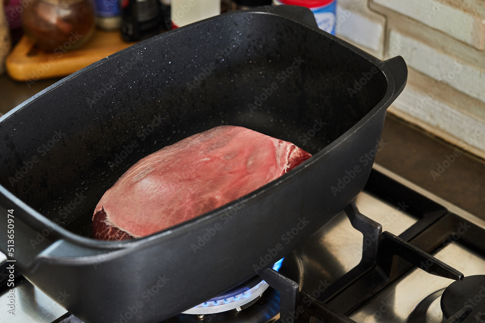 Wall mural Piece of meat is roasted in rectangular pot for cooking over fire on gas stove