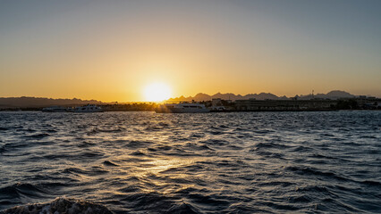 Sunset over the Red Sea. The sun is low. Silhouette of a mountain range against an orange sky. Ripples and highlights on the water. Egypt. Safaga