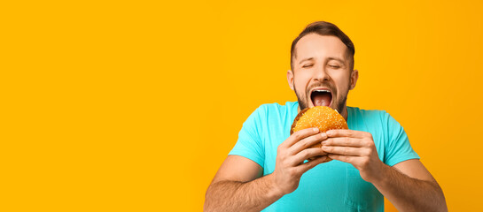 Man eating tasty burger on yellow background with space for text