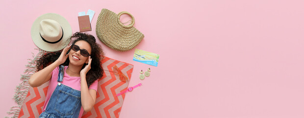 Young female African-American tourist with beach accessories on pink background with space for...