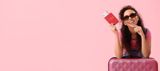 Young African-American woman with passport, tickets and suitcase on pink background with space for...