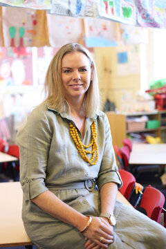 Female school teacher sitting on a classroom desk