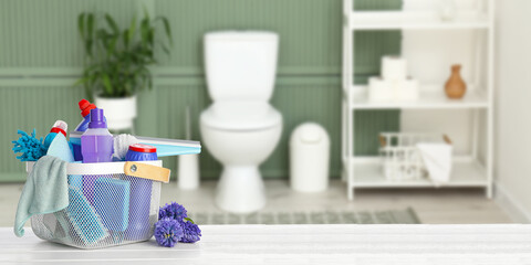 Set of cleaning supplies and spring flowers on table in bathroom