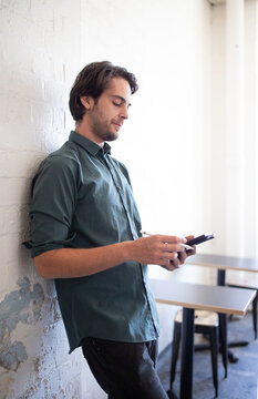 Man leaning against a wall looking at e-device in office