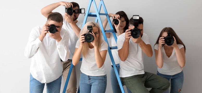 Group of young photographers near ladder on light background