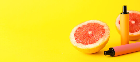 Modern electronic cigarettes and grapefruit on yellow background with space for text