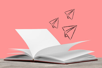 Open book on table against pink background with drawn paper airplanes