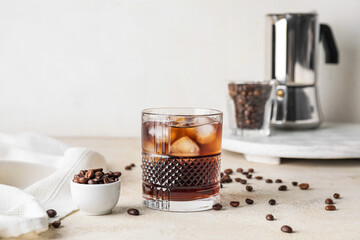 Glass of cold brew and coffee beans on table against light background