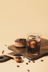 Wooden board with glass of cold brew and coffee beans on color background