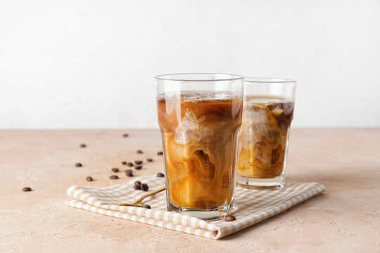 Glasses of cold brew coffee on beige table against light background