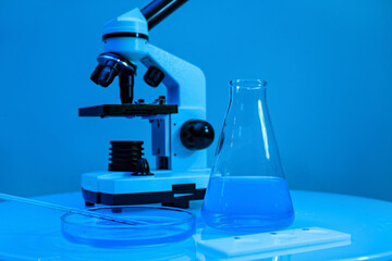 Different laboratory glassware with samples and microscope on table near blue wall
