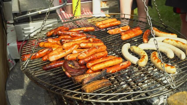 Chef flips sausages Bratwurst roasting with cooking tongs. Street food for picnic and camping. BBQ grilling frankfurt beef sausage. Grilled weisswurst fried and smoked in charcoal grills. 4k footage