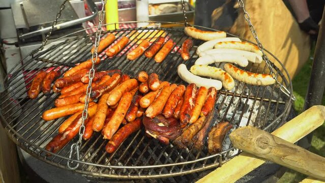 Adding charcoal to the grill. Bratwurst roasting on barbecue grill. BBQ grilling frankfurt beef sausage. Street food for picnic and camping. Grilled weisswurst fried and smoked in charcoal grills. 4k
