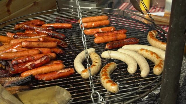 Sausages Bratwurst roasting on barbecue grill outdoors. Street food for picnic and camping. BBQ grilling frankfurt beef sausage. Grilled weisswurst fried and smoked in charcoal grills. FullHD