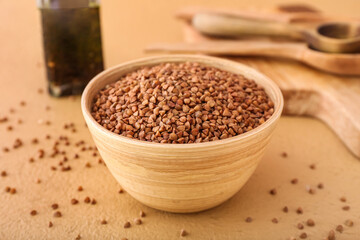 Wooden bowl with buckwheat grains on color table