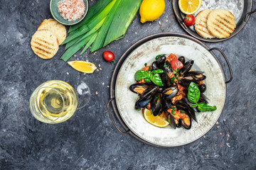 Fine dining in a seafood restaurant: a big dish of mussels with bottle of white wine with two wine glasses, on dark background. Restaurant menu, dieting, cookbook recipe top view