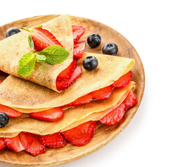 Plate of thin pancakes with strawberries and blueberries on white background