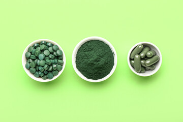 Bowls with spirulina pills and powder on green background