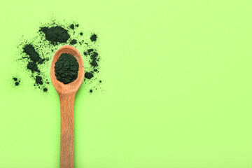 Wooden spoon with spirulina powder on green background