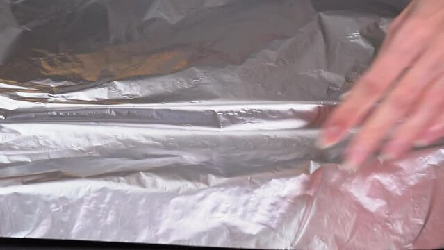 Woman covering baking sheet with foil. View from above of chef hands covers baking sheet with aluminum foil slow motion. High quality FullHD footage