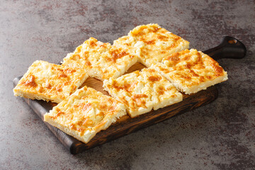 Alevropita Greek pie consisting of a thin batter that is sprinkled with feta cheese close-up on a wooden board on the table. Horizontal