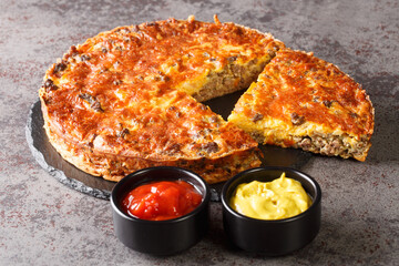 Homemade crispy cheeseburger pie served with sauces close-up on a slate board on the table. horizontal