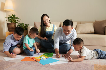 Smiling parents and their three sons drawing pictures on floor together