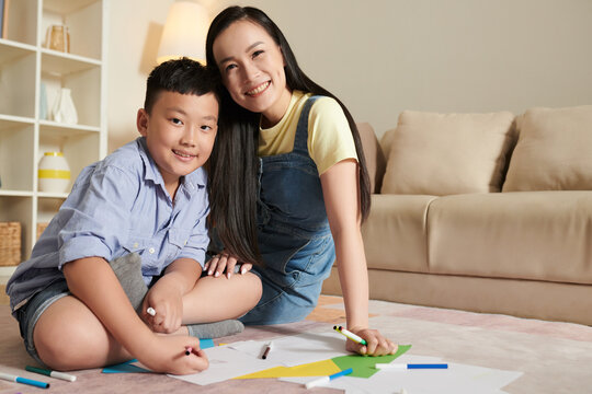 Smiling Asian mother and son sitting on floor and drawing pictures